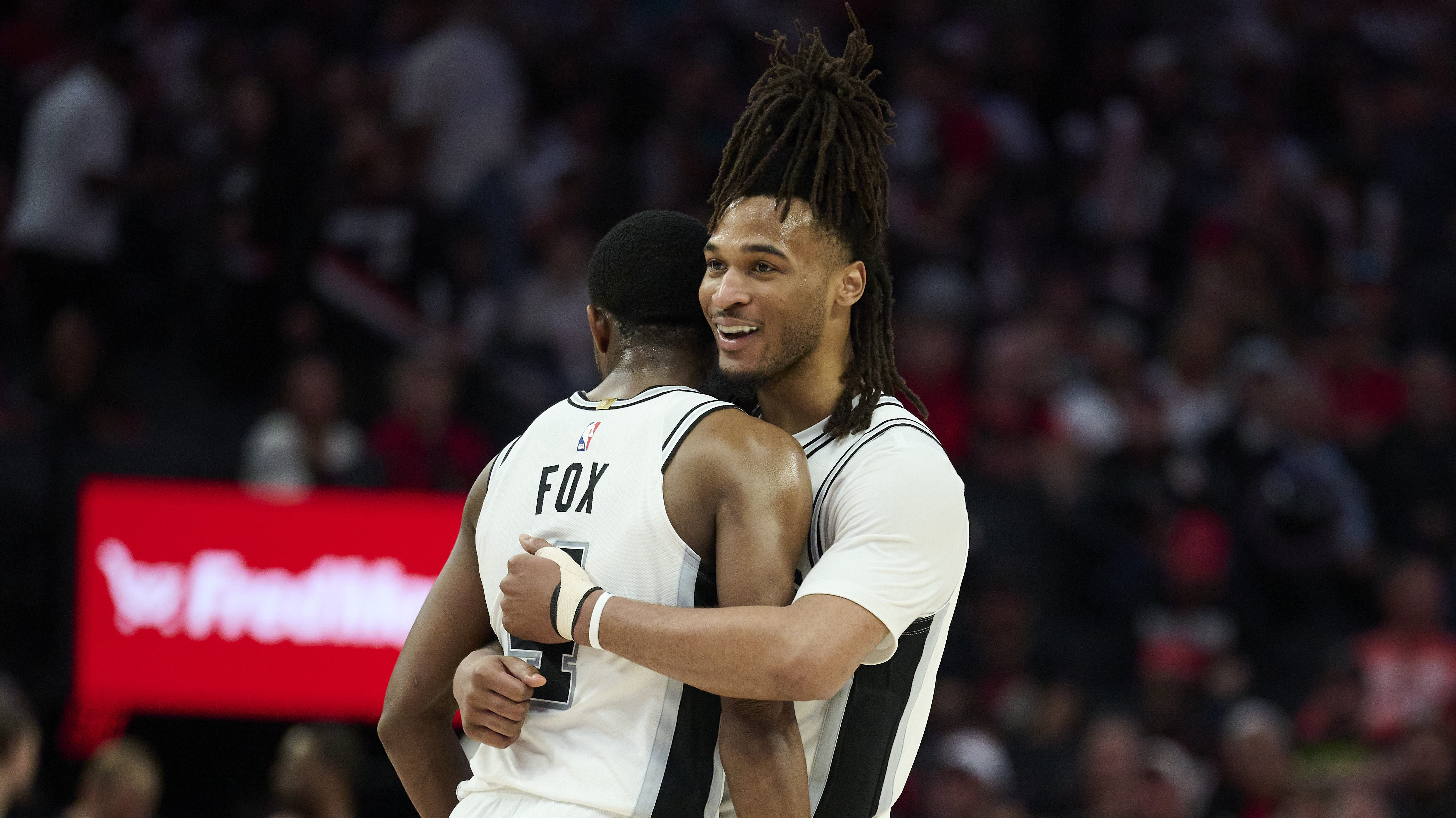 San Antonio Spurs guards Stephon Castle and De'Aaron Fox hug at midcourt.