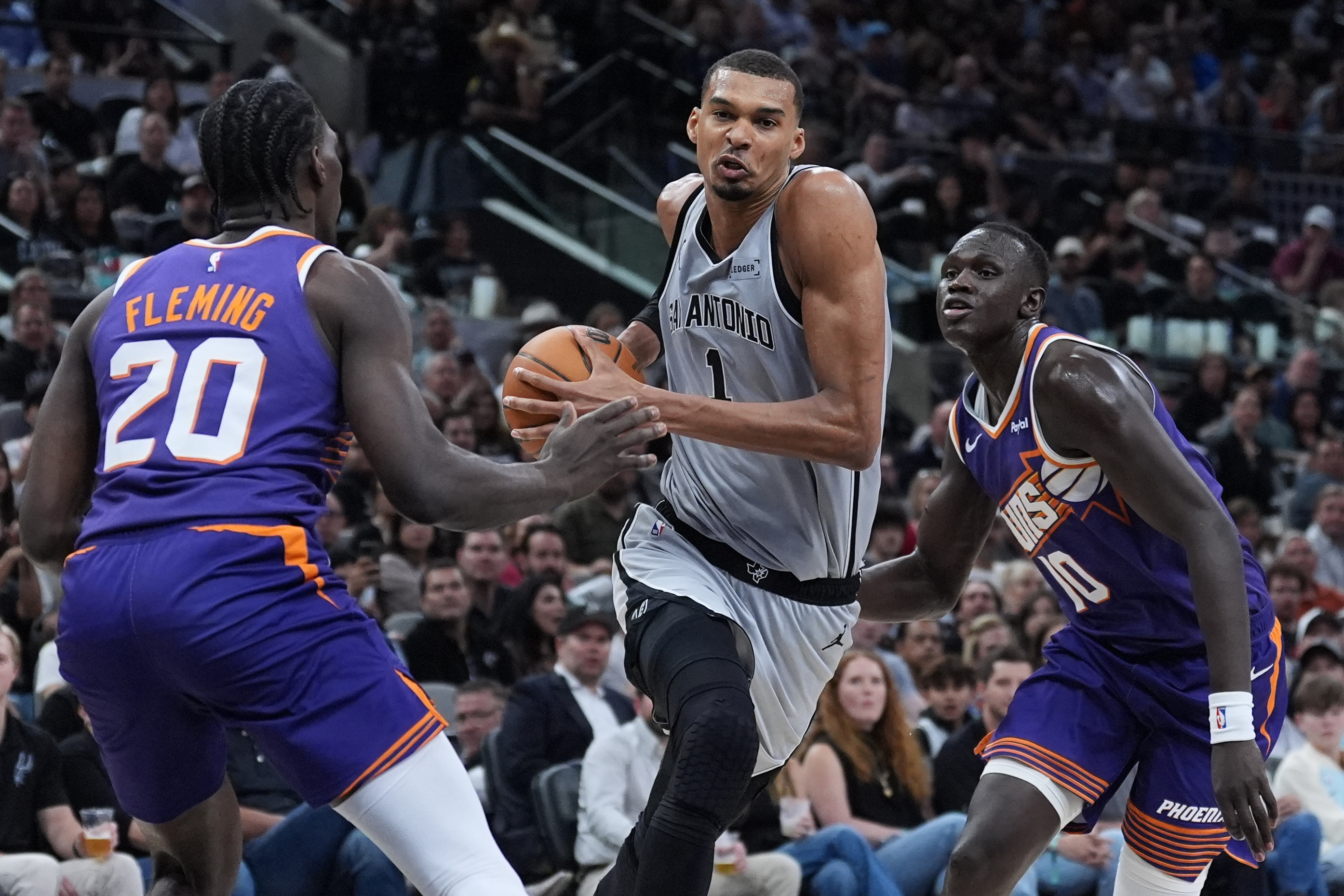 San Antonio Spurs forward Victor Wembanyama (1) drives between Phoenix Suns forward Rasheer Fleming (20) and center Khaman Maluach (10) during the second half of an NBA basketball game in San Antonio, Thursday, March 19, 2026. (AP Photo/Eric Gay)